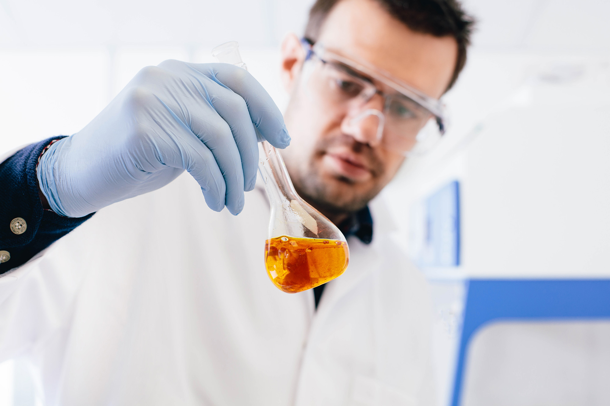 Scientist holding glass beaker containing clear orange liquid
