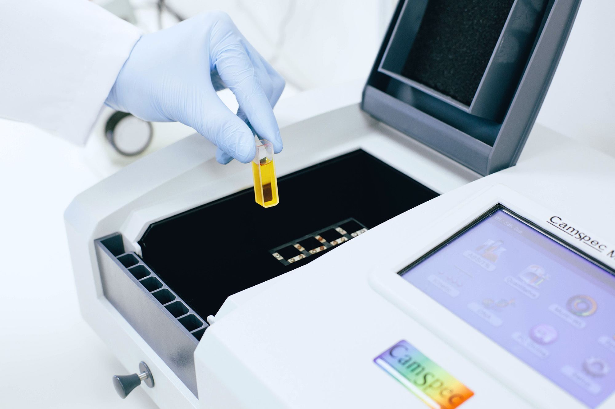 Photo showing a scientist putting a small orange yellow liquid inside of a UV spectrometer CamSpec machine.
